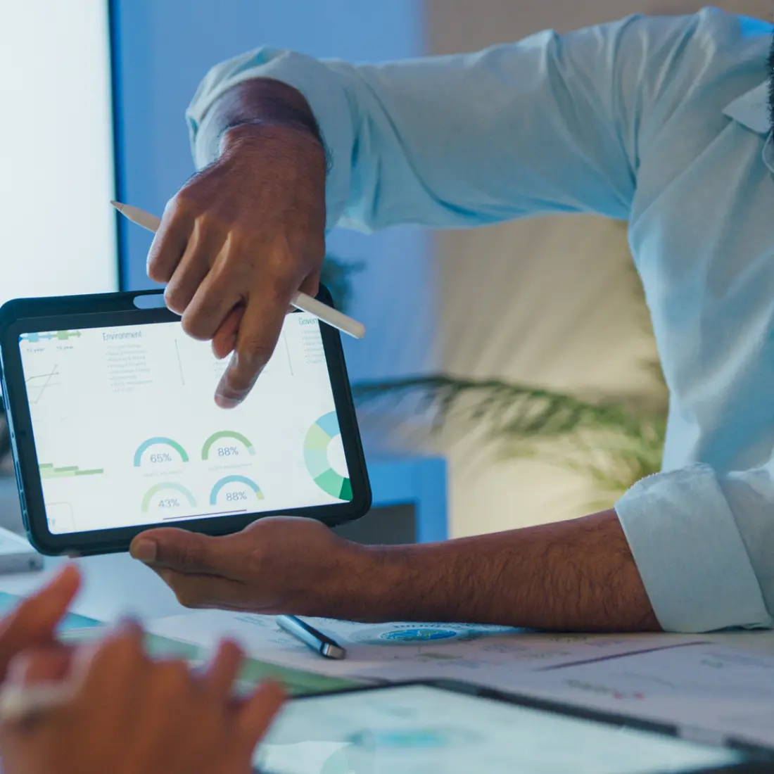 Ein Projektleiter zeigt seinen Arbeitskollegen Graphiken und Statistiken auf einer Tablet.
